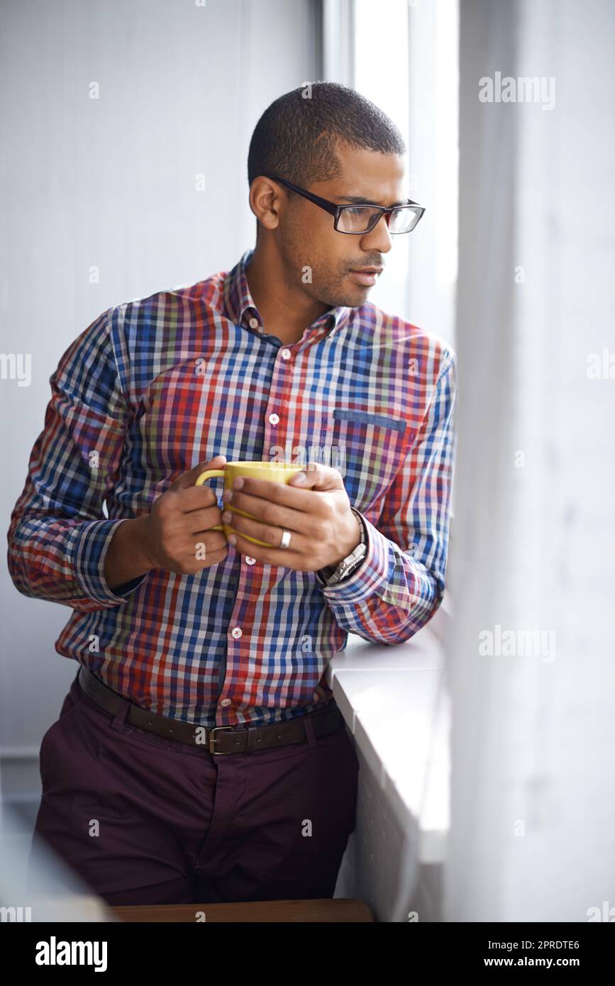 Young, professional and confident black business man thinking of ideas for a project. Serious African American male on a break contemplating as he looks at the view from work during a coffee break Stock Photo