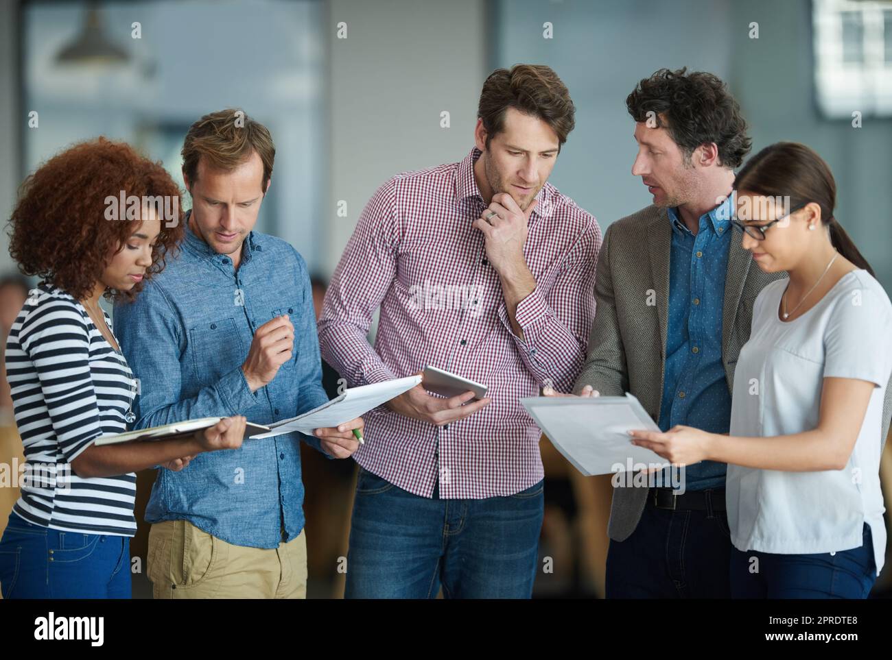 Colleagues talking about paperwork while standing in the office together. Business people working together to discuss strategy while using wireless devices. Tech savvy ways to save time in your job. Stock Photo