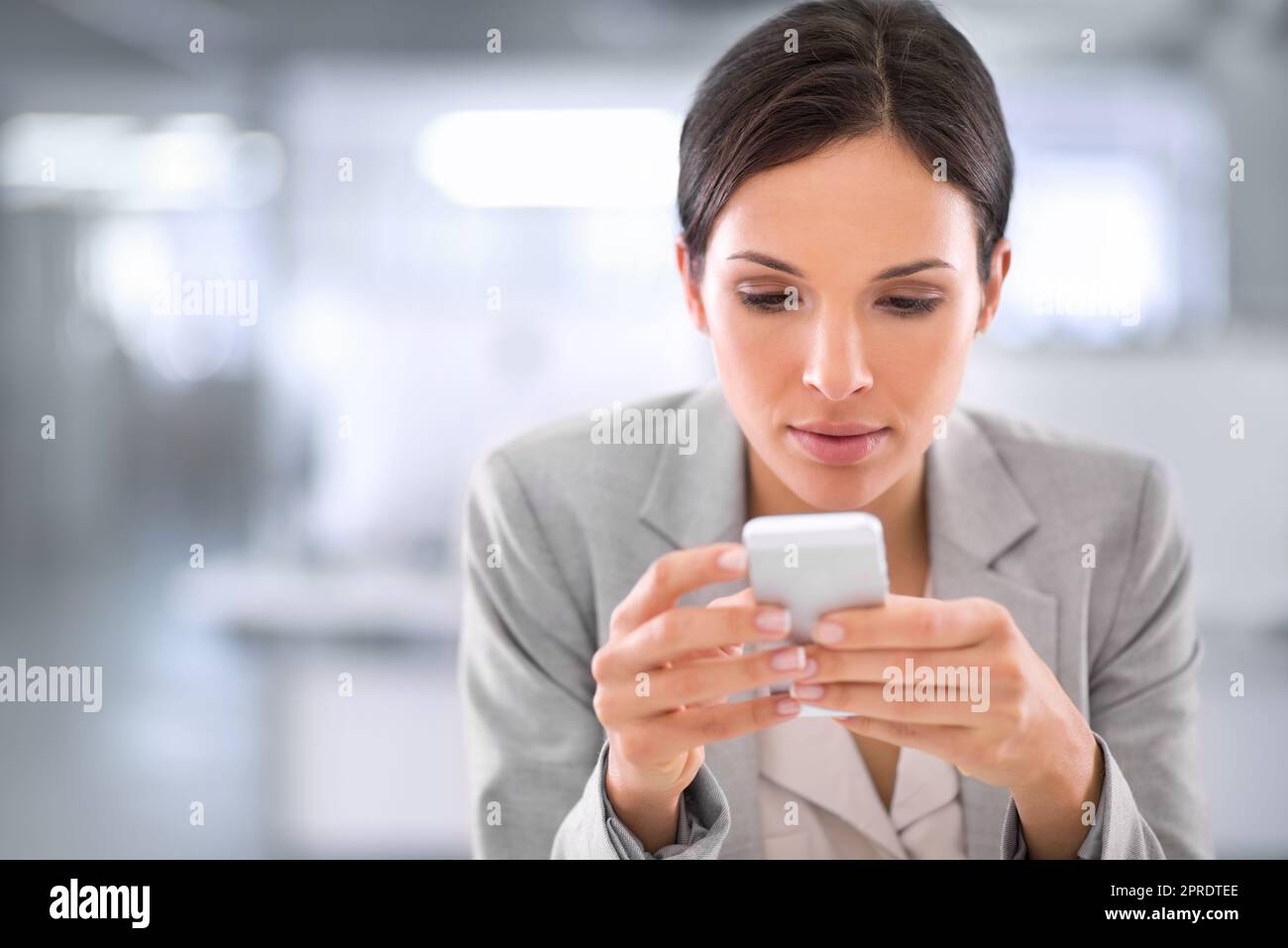 Young woman browsing social media on a phone at work in a modern office. Serious female interested and curious about fake news or stories. Lady reading updates on the internet while on a break Stock Photo