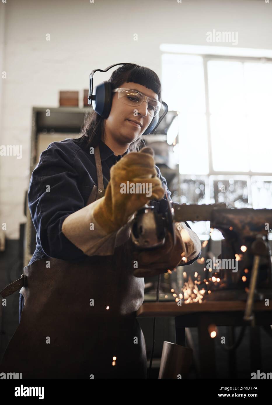 Smoothing it out. an attractive young female artisan using an angle grinder in her workshop. Stock Photo