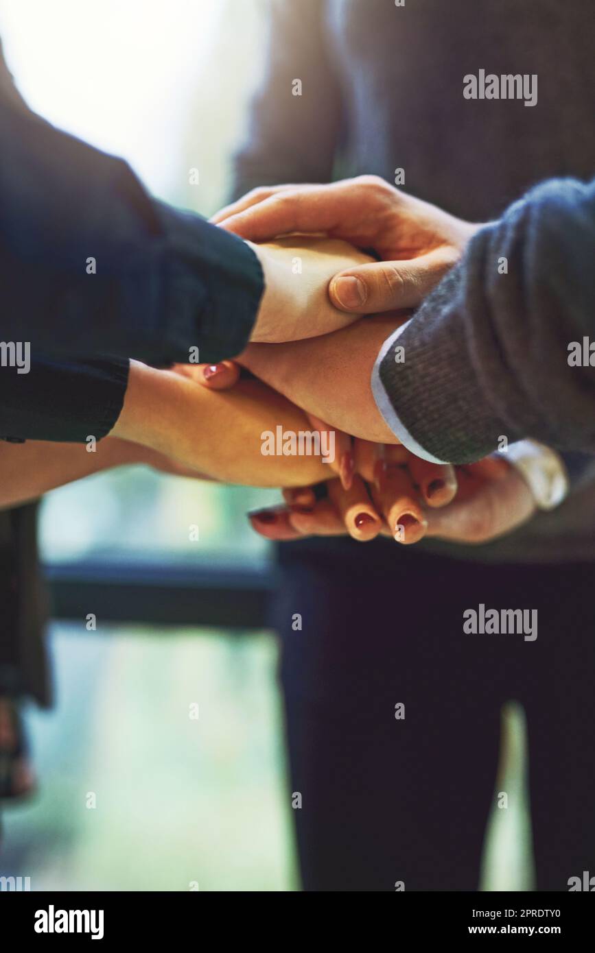 In order to succeed in business, we must unite. a group of unrecognizable businesspeople huddled together with their hands piled on top of each other in an office. Stock Photo