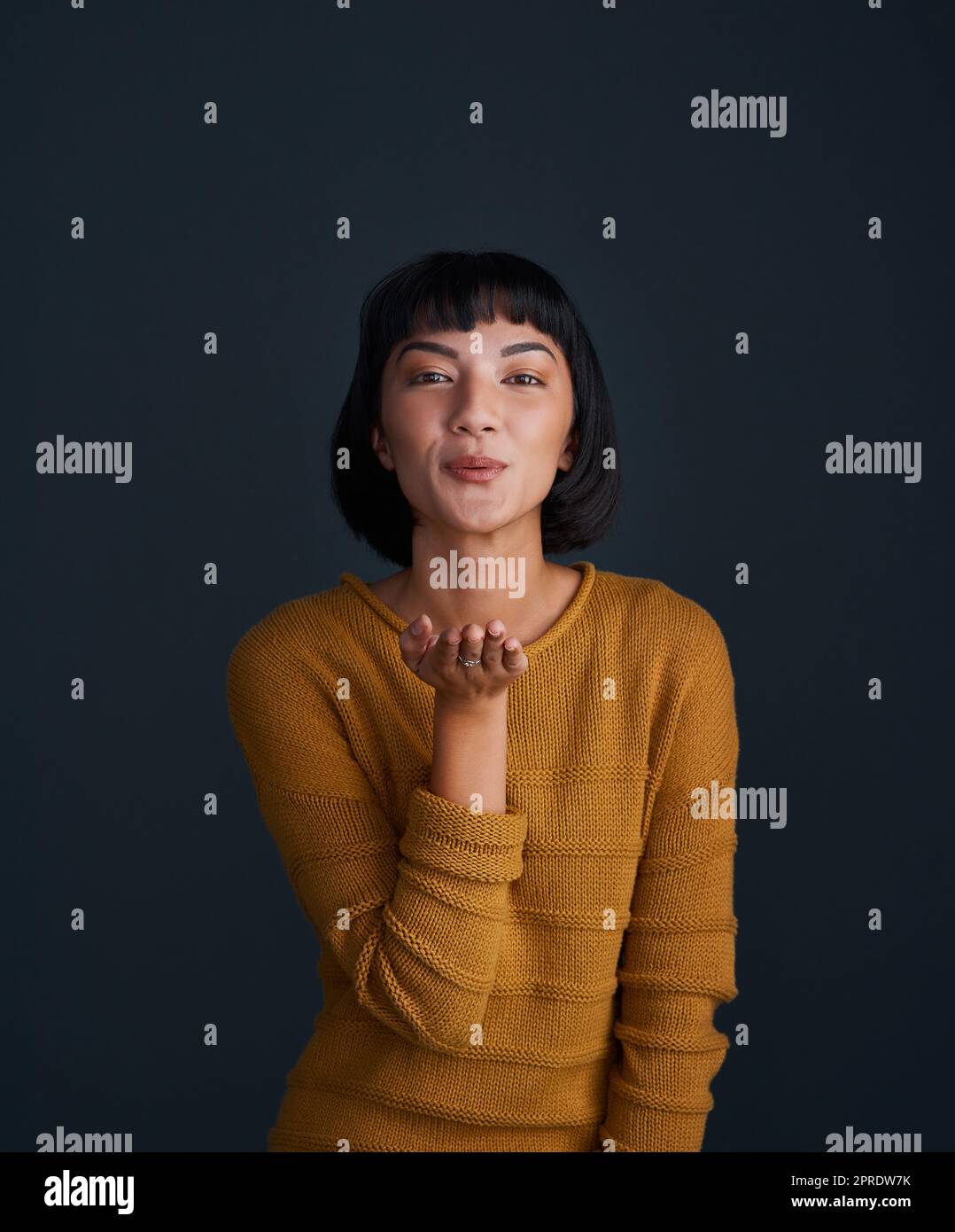 Mwah Its all for you. Studio portrait of an attractive young woman blowing kisses against a dark background. Stock Photo