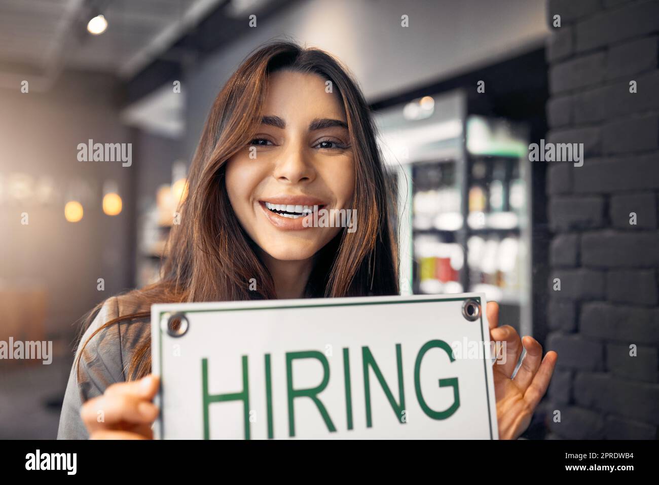 Looking for a job. Cropped portrait of an attractive young woman holding up a hiring sign while standing in her coffee shop. Stock Photo