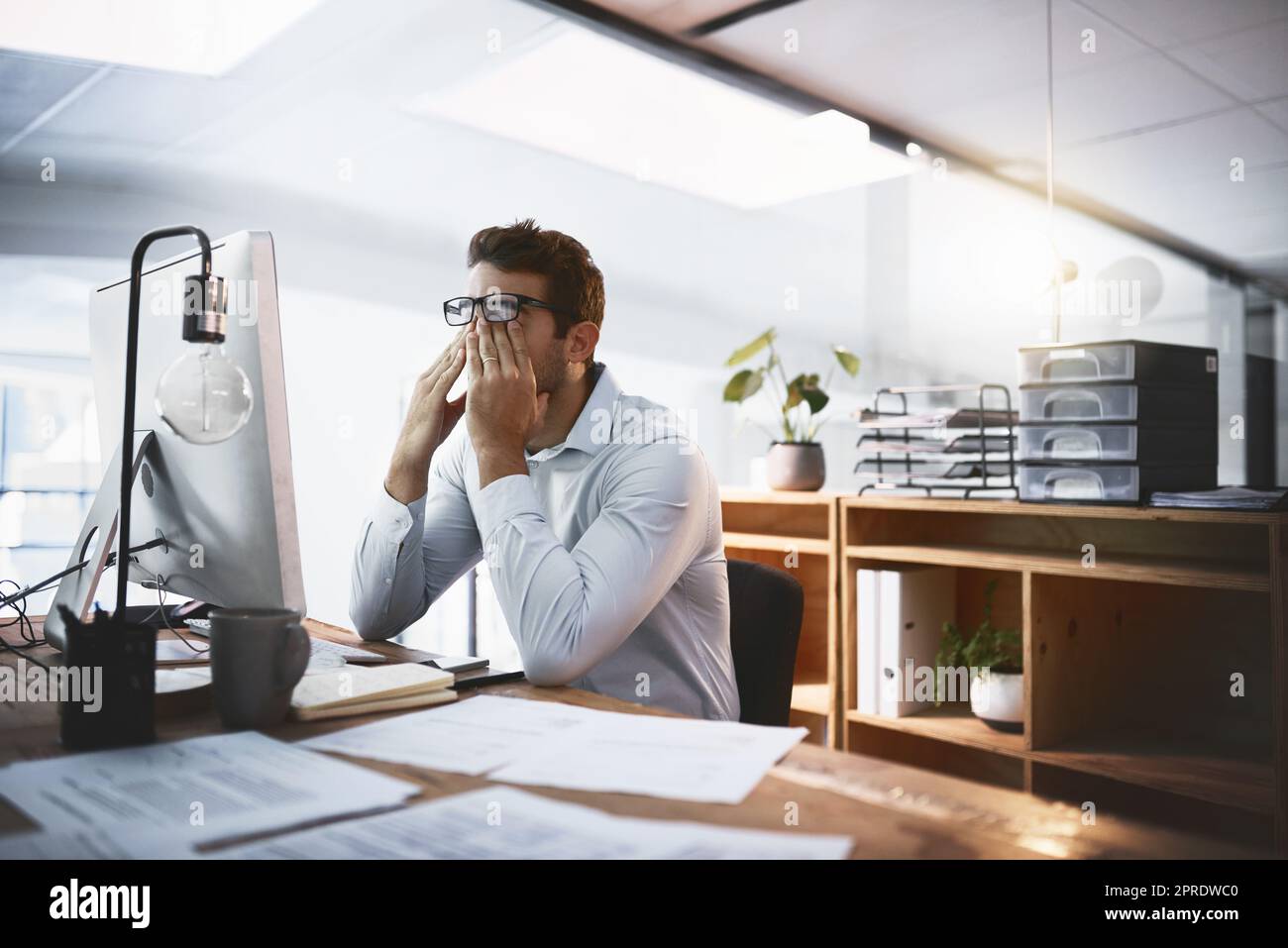 My brain just cant function anymore. a young businessman looking exhausted while working late on a computer in an office. Stock Photo