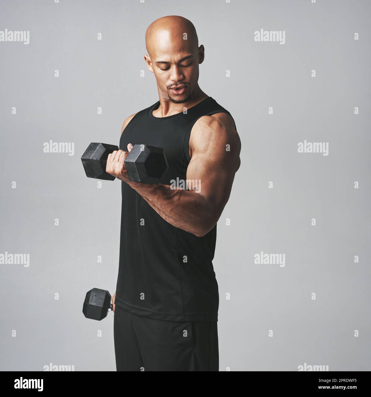 Building his biceps. Studio shot of an athletic young man working out with dumbbells against a grey background. Stock Photo