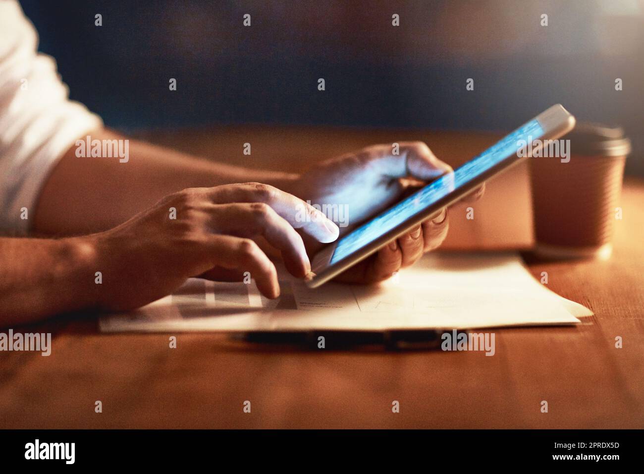 Closeup of a persons hands holding and scrolling on a digital tablet planning late in the evening at night. Modern man working online with a touchscreen display device, at desk of workplace Stock Photo