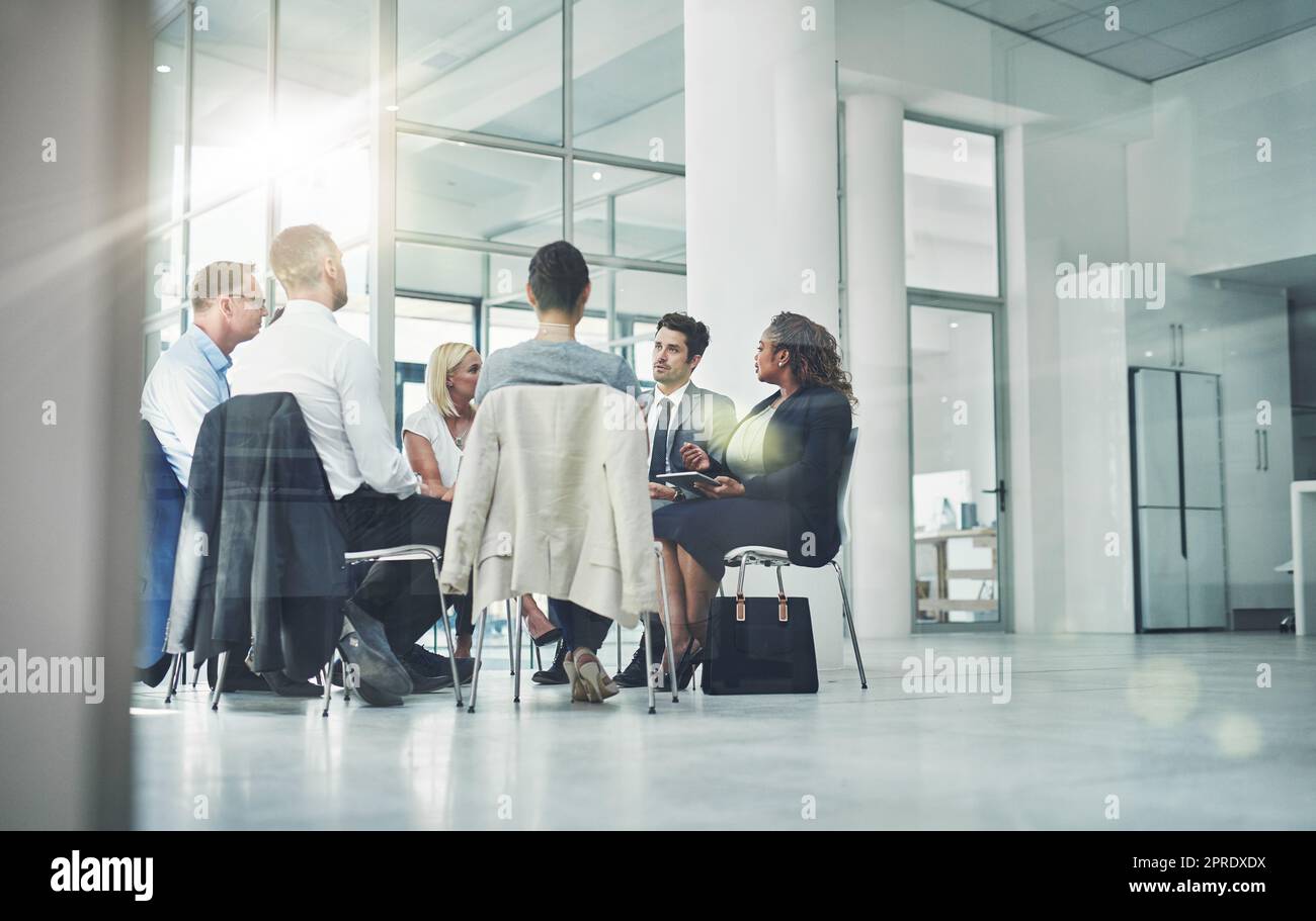 Group of diverse coworkers talking together while sitting in a circle in an office. Employees having a team business meeting discussion for counseling or support group at a corporate workplace. Stock Photo