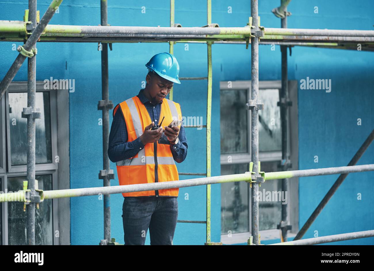 Male construction worker working checking a digital building plan on a phone. Busy urban development builder looking at buildings planning data to give industry information on a two way radio Stock Photo