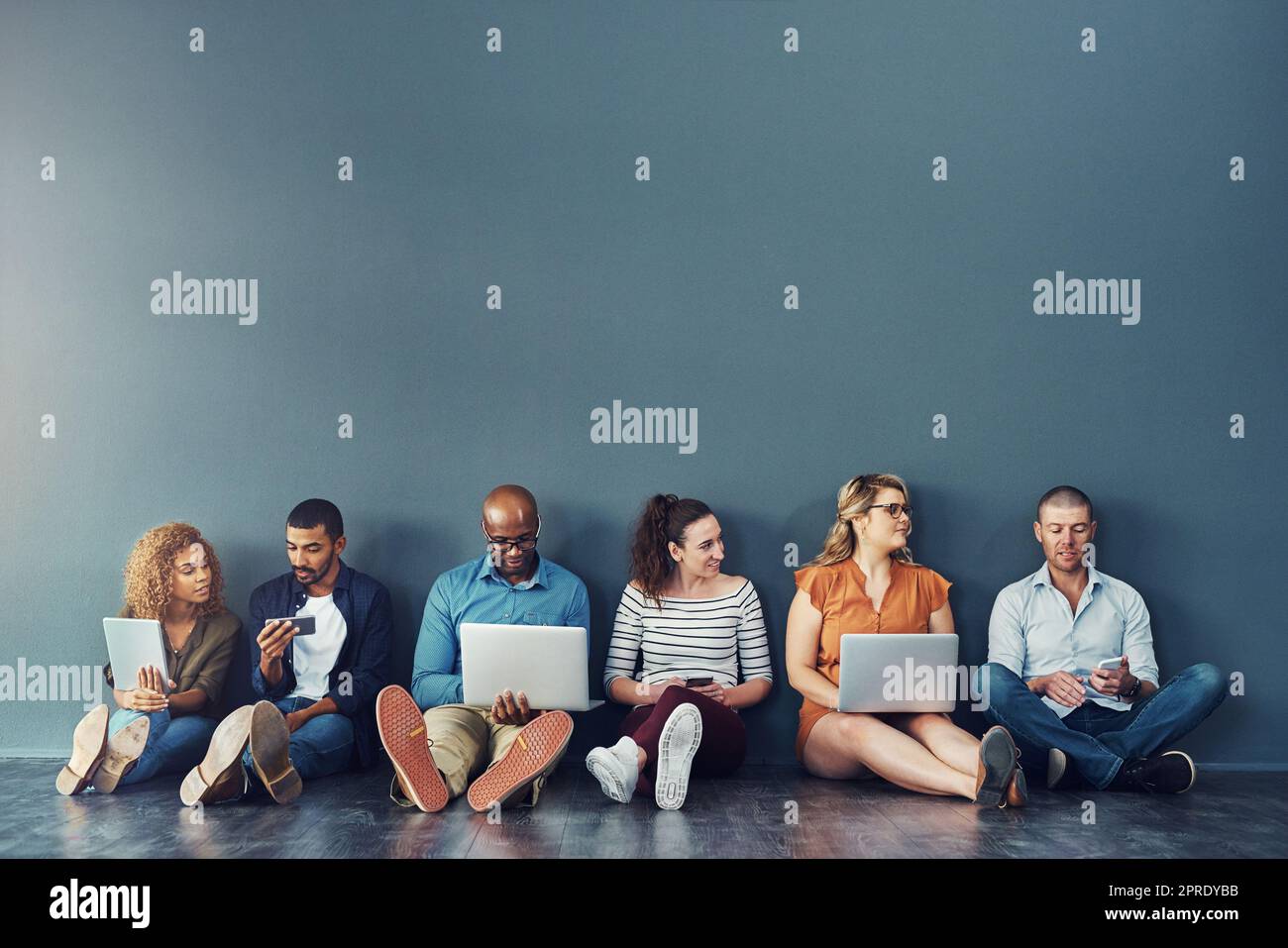 Diverse digital team exploring online platform on many devices, sitting against copy space together. Social advertising and global networking, collaborating with technology, connecting global network Stock Photo