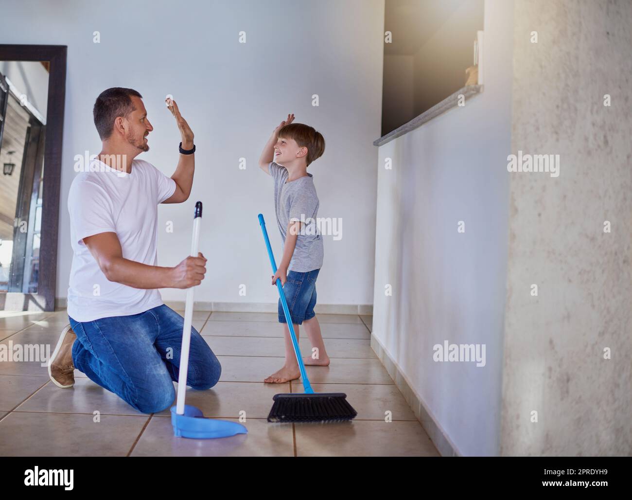 Good job buddy. a father and his little son high fiving each other while sweeping the floor at home. Stock Photo