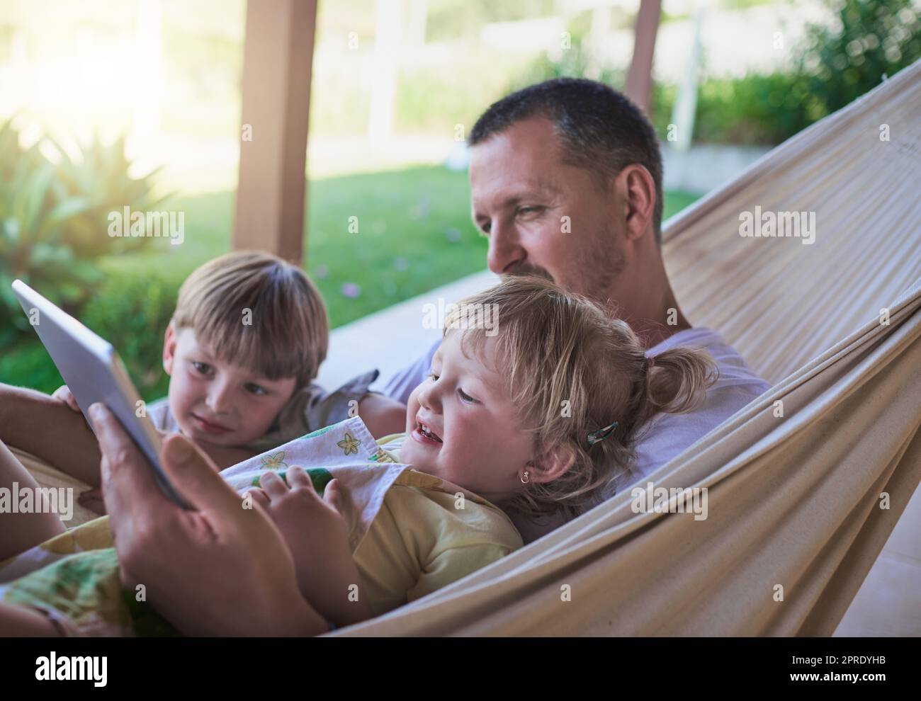 Dads always willing to watch cartoons with his kids. a father and his two little children using a digital tablet while relaxing on a hammock outdoors. Stock Photo