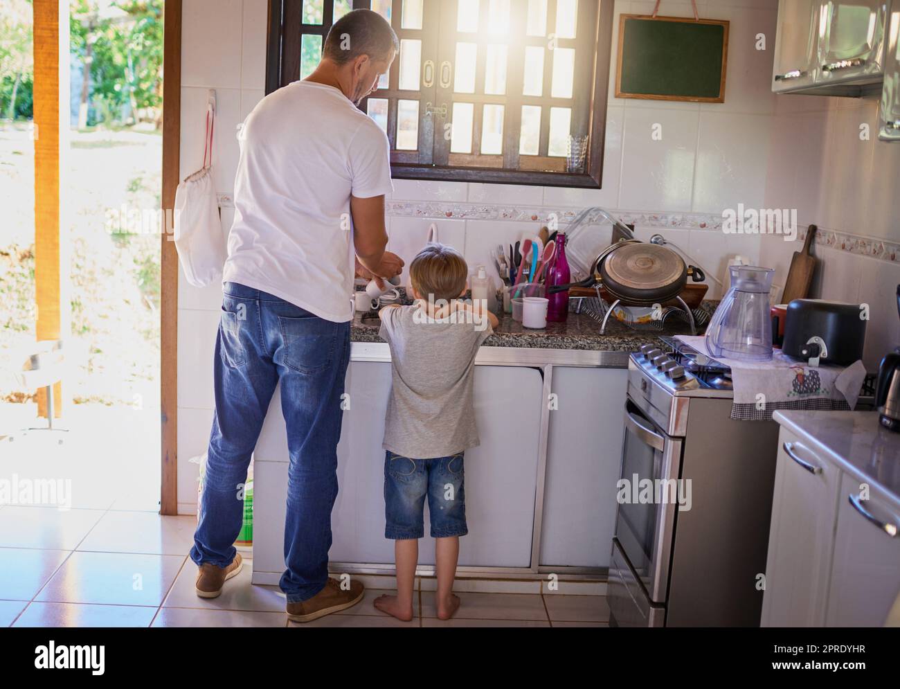 Dads been teaching him how to do the dishes. Rearview shot of a father and his little son washing dishes together at home. Stock Photo