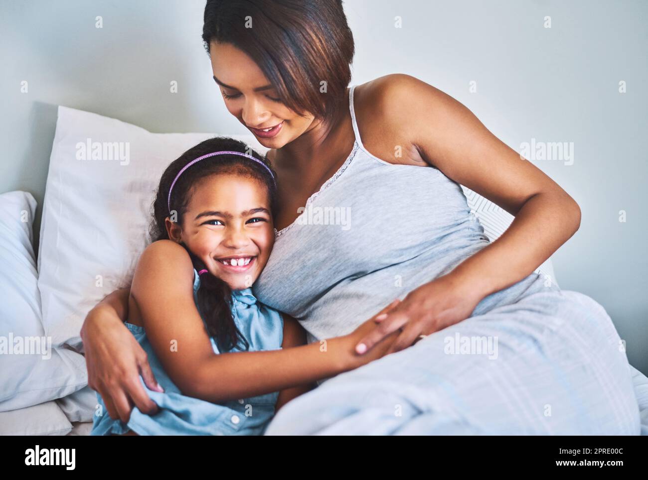 You will always be my firstborn. Portrait of a cheerful little girl relaxing on the bed with her pregnant mother at home during the day. Stock Photo