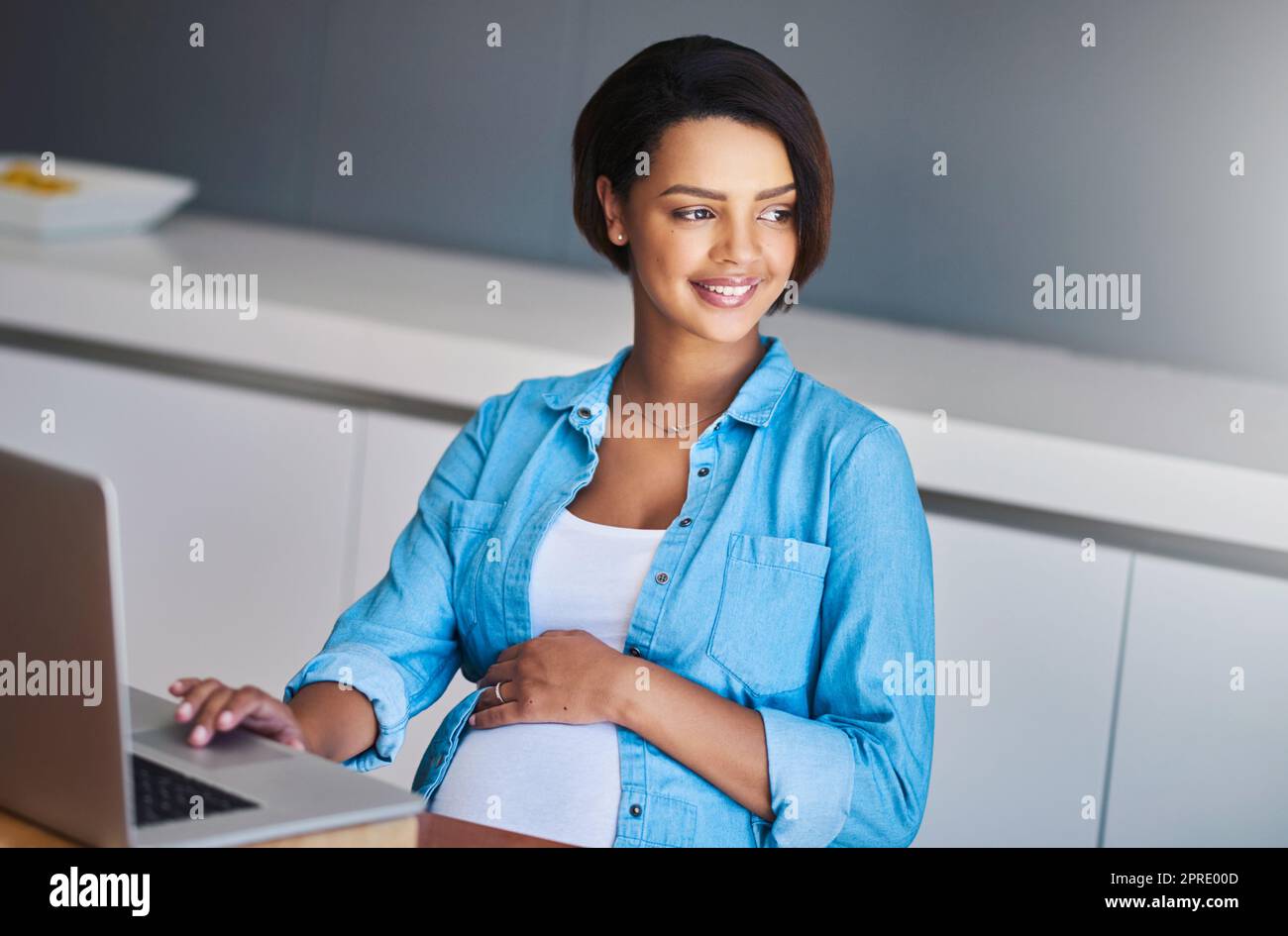 Thank goodness the days of stressful commuting is behind me. a pregnant young woman using a laptop while working from home. Stock Photo