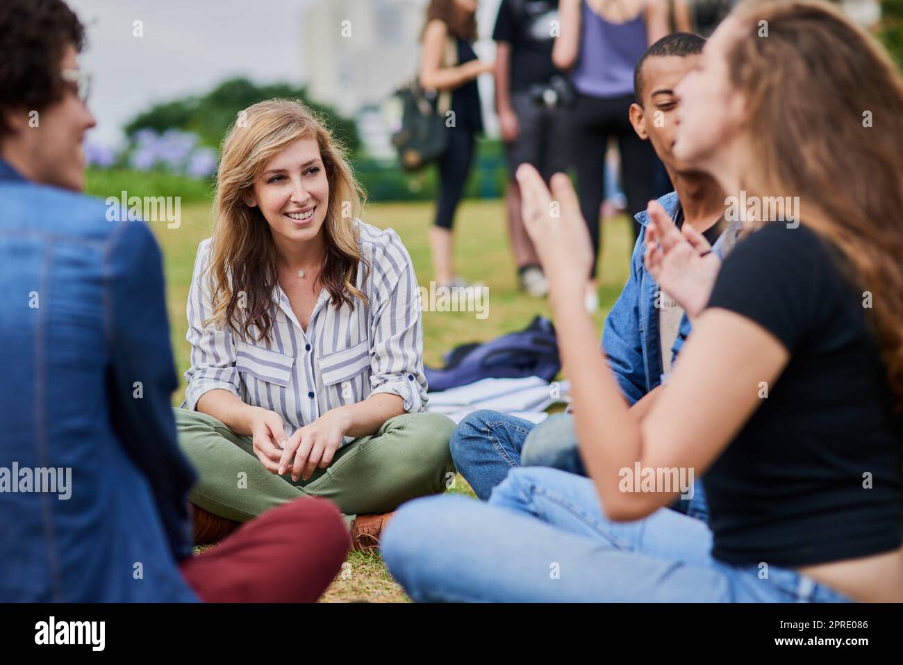 Chatting about life. a group of young students studying together while being seated in a park outside during the day. Stock Photo