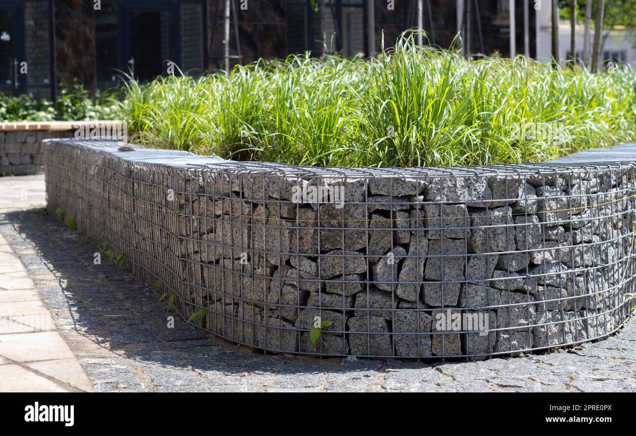 Basket support wall made of granite gabion. Gabions in the garden. Modern Gabion fence with stones in wire mesh. Gabion wire mesh fencing with natural stone and shrubs. Stock Photo