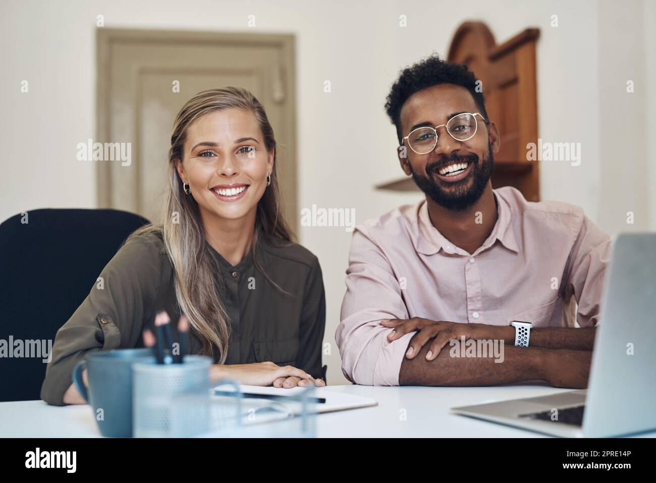 Happy diverse employees working together on a project sitting in an office table satisfied with the partnership. Portrait of young colleagues with a positive mindset smiling about business growth Stock Photo
