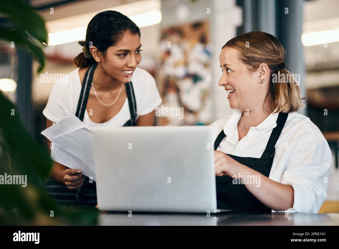 Small business owner working on a budget strategy or ordering stock online with an employee using a laptop in her store. Female entrepreneur talking to a worker about startup growth and sales Stock Photo