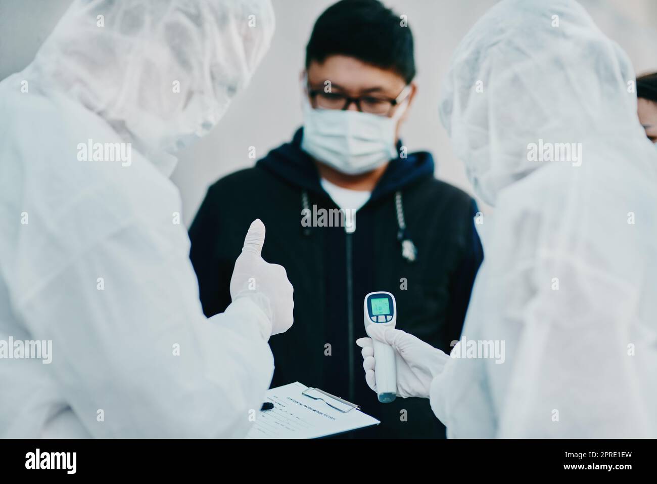 Negative covid test and thumbs up for young man from healthcare worker after testing for virus. Medical professionals in hazmat suits taking temperature tests during disease outbreak or pandemic Stock Photo
