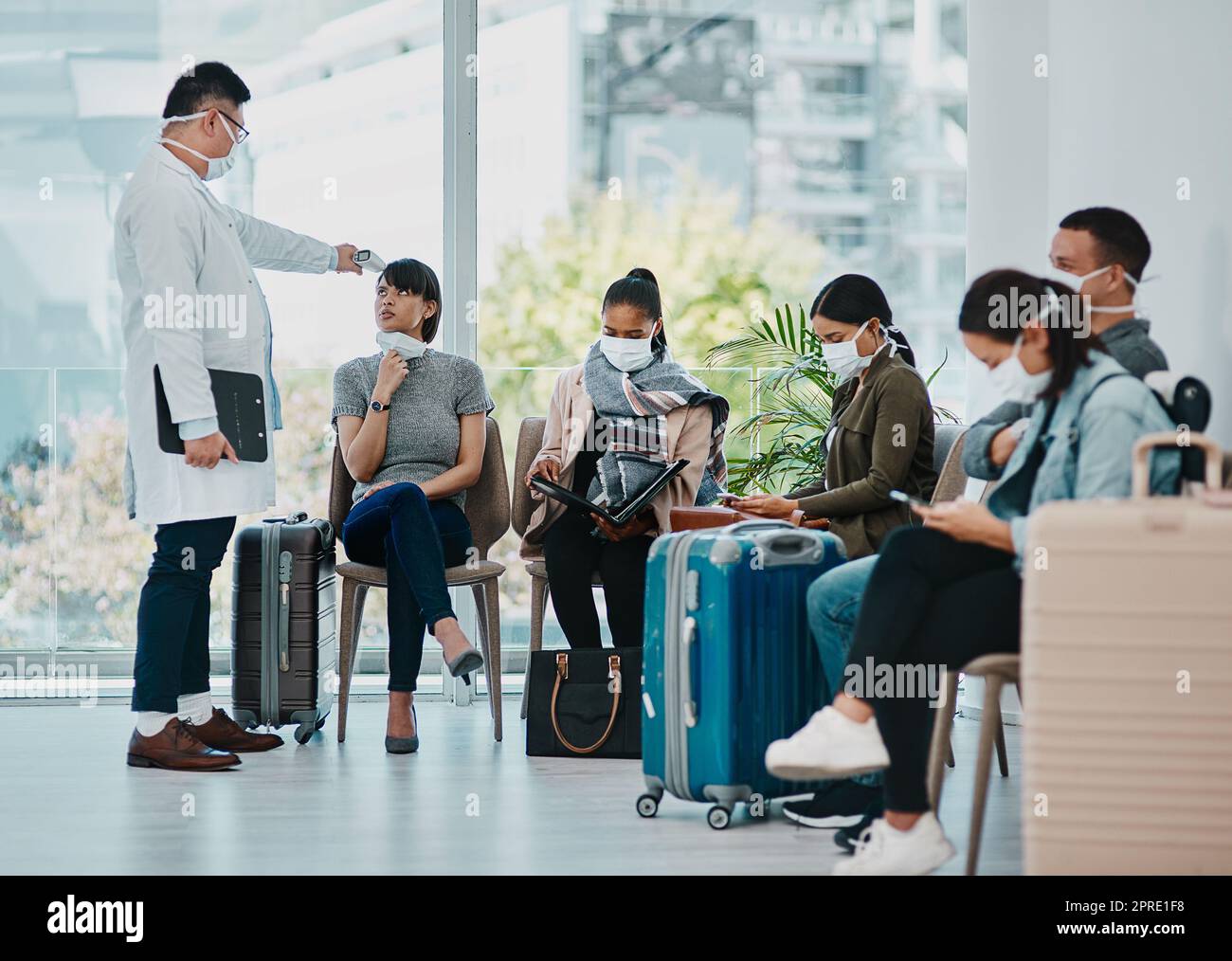Covid doctor taking temperature of travel passengers in covid masks during tourism in an airport with an infrared thermometer. Medical professional following safe protocol in an epidemic or outbreak Stock Photo