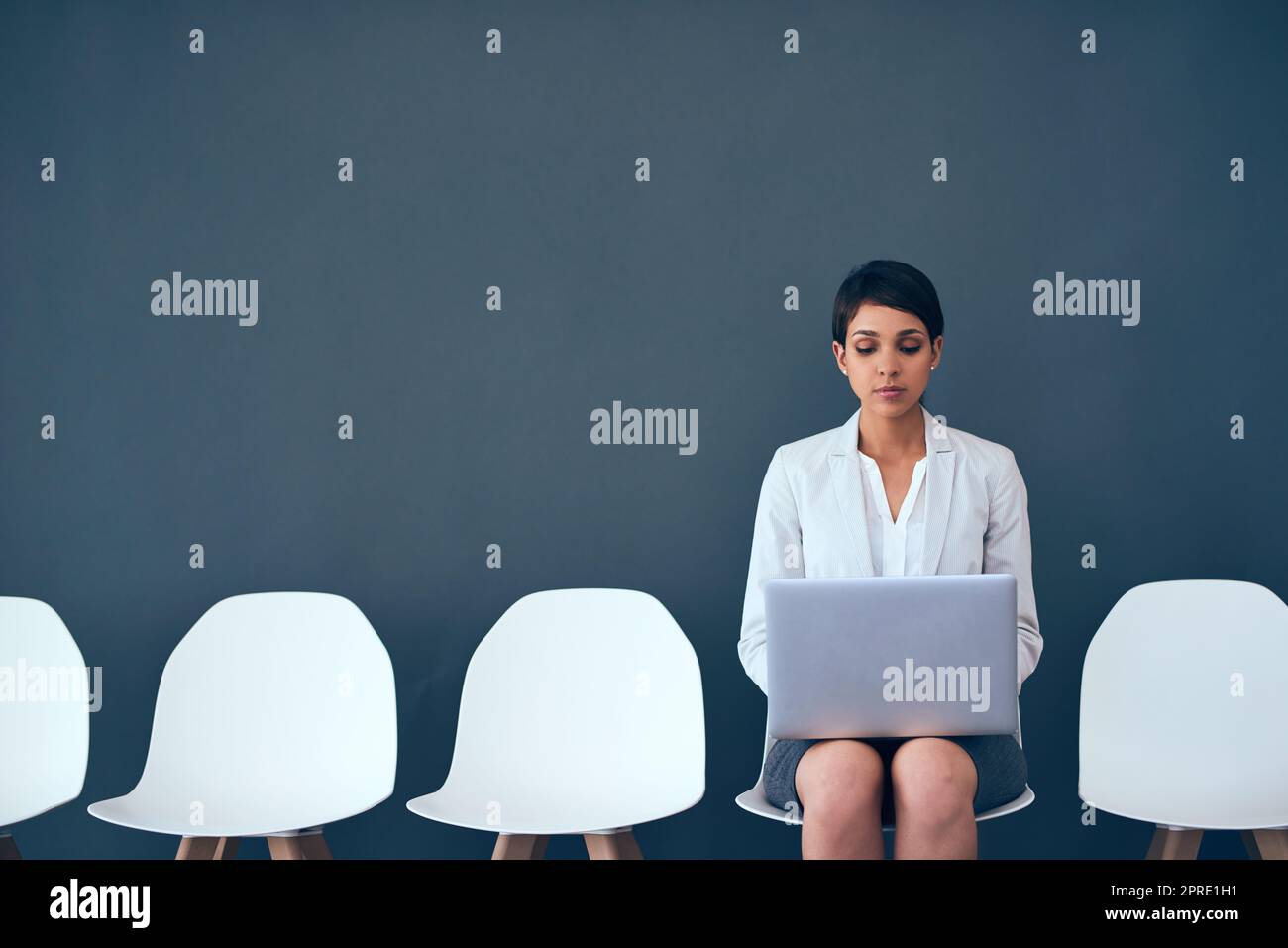 Shes the last one waiting. Studio shot of an attractive corporate businesswoman using a laptop while waiting in line against a gray background. Stock Photo