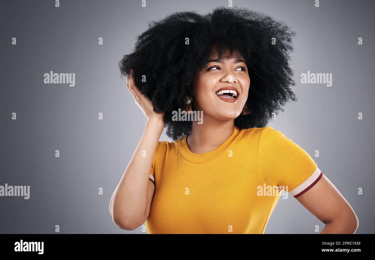 She just loves her big hair. Studio shot of an attractive young woman posing against a grey background. Stock Photo