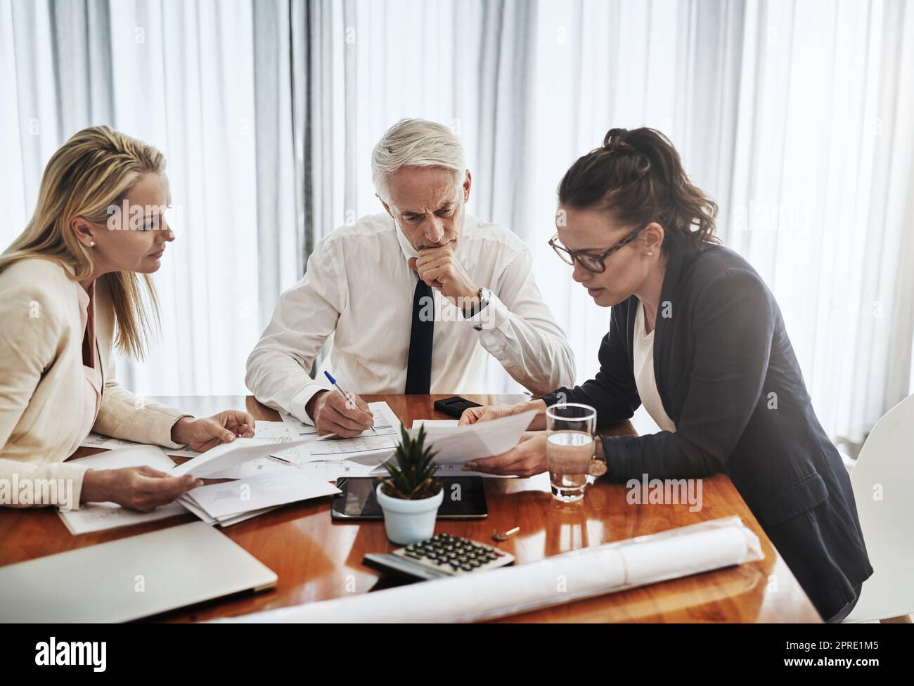 Thinking as a group. a group of architects working together on blueprints of a house around a table inside of a building. Stock Photo