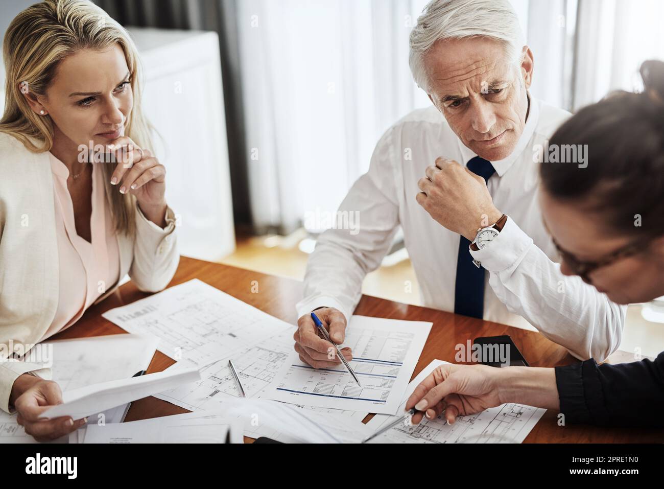 Everything seems to be going accordingly. a group of architects working together on blueprints of a house around a table inside of a building. Stock Photo