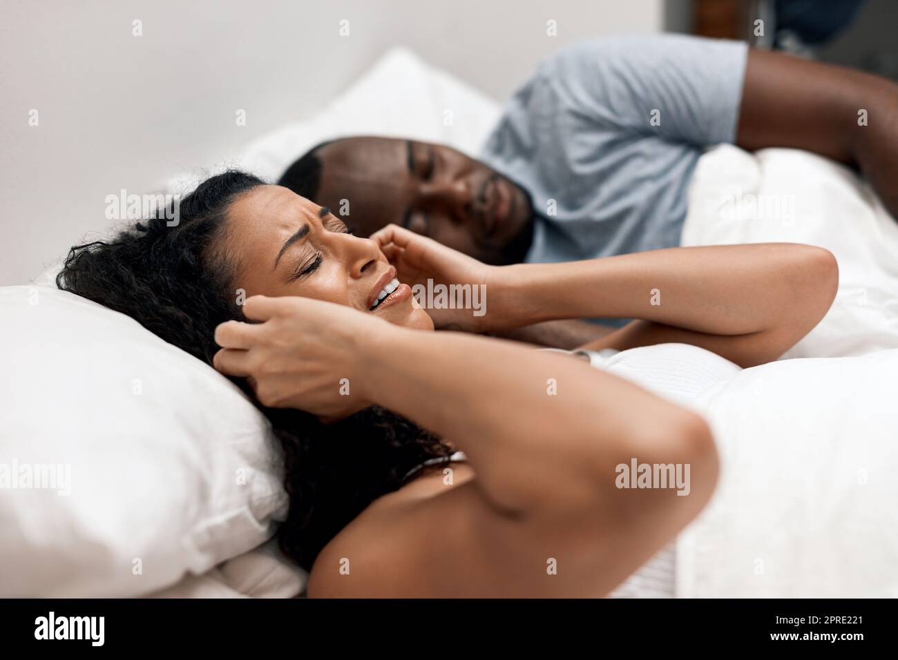 How am I going to get some sleep now. an uncomfortable looking young woman  holding her ears closed because of her husbands snoring in bed at home  Stock Photo - Alamy