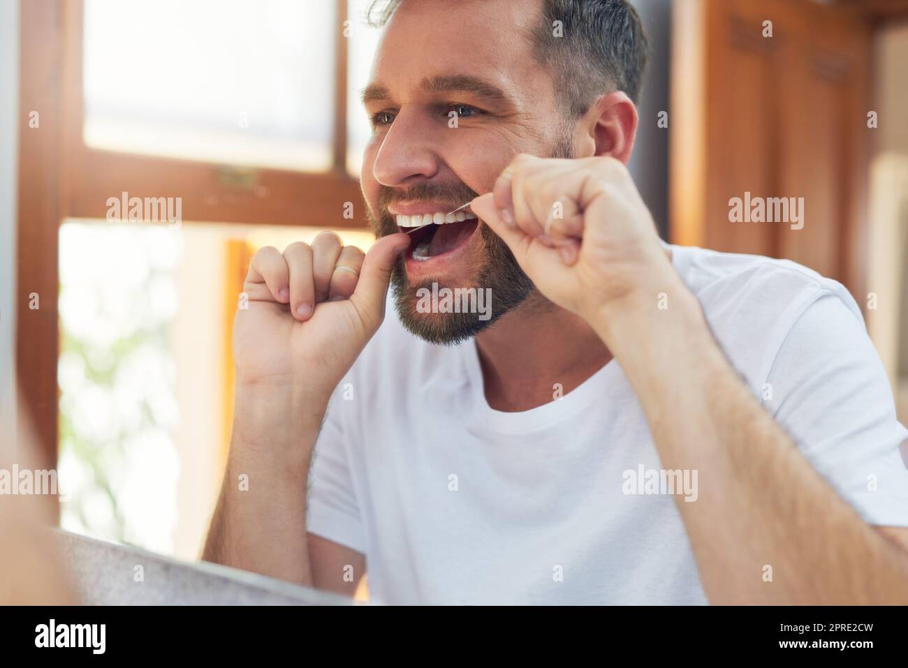 Take your dental hygiene routine a step further by flossing. a handsome young man flossing his teeth in the bathroom. Stock Photo
