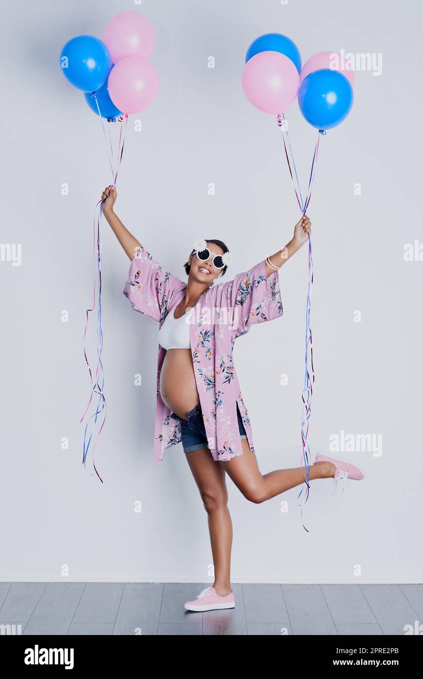 Overjoyed, I dont mind if its a girl or boy. Studio shot of a beautiful young pregnant woman holding blue and pink balloons against a gray background. Stock Photo