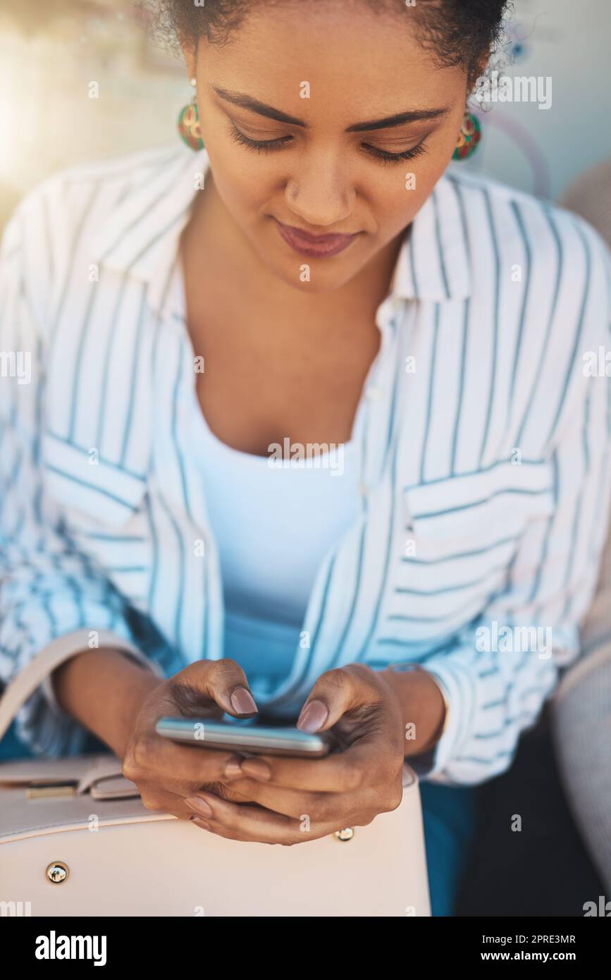 Lets see what my friends are up to. a focused young woman texting on his cellphone while being seated outside during the day. Stock Photo