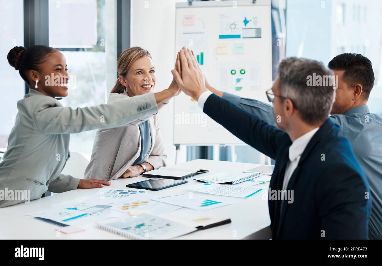 High five, success and motivated business group celebrating innovation deal, promotion or profits. Diverse executive team with growth mindset cheering and analyzing report data in boardroom meeting Stock Photo
