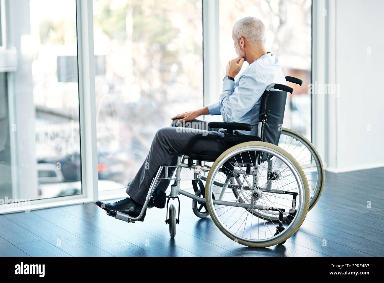 Taking a moment to ponder by himself. a mature man sitting in a wheelchair and looking out the window. Stock Photo