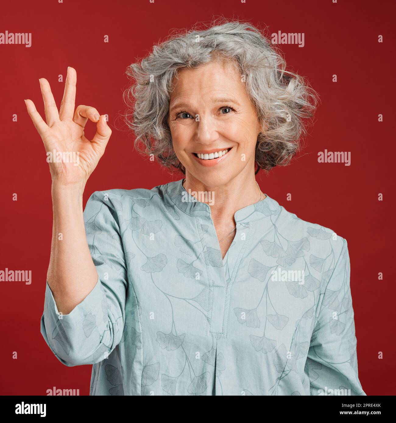 Good, perfect and okay with a senior woman hand gesture or sign in support or positive backing in studio against a red background. Portrait of a mature female looking motivated, happy and smiling Stock Photo