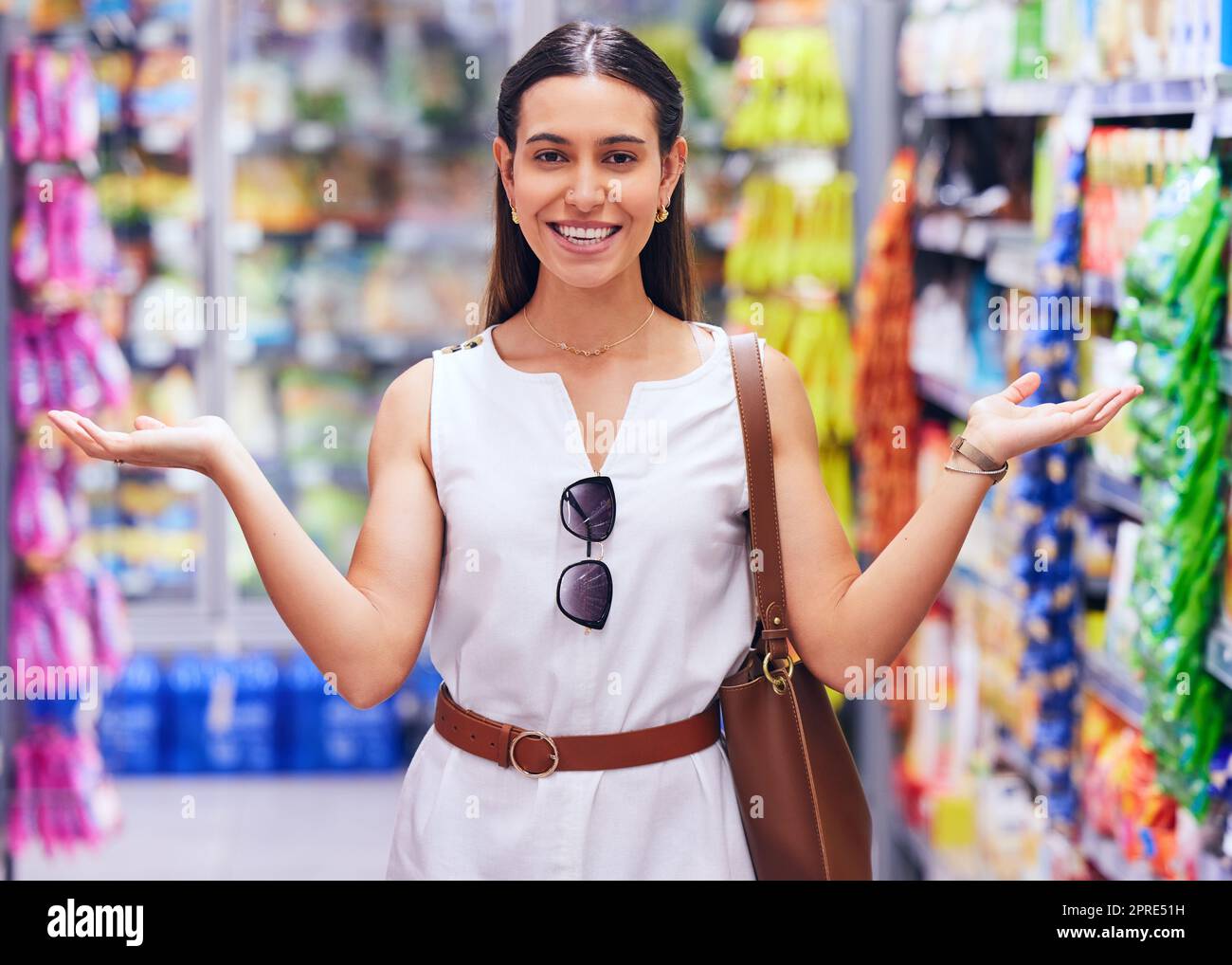 Shopping, retail and consumerism with a female customer standing in a grocery store, shop or supermarket aisle. Portrait of a young woman gesturing with products packed on shelves in the background Stock Photo