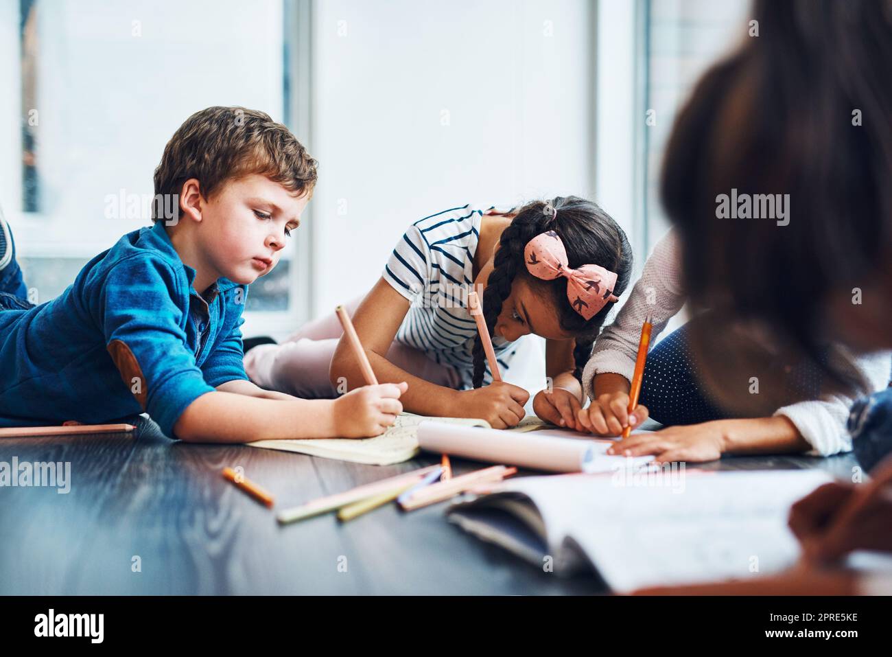 They love being creative. kids coloring in while lying on the floor. Stock Photo