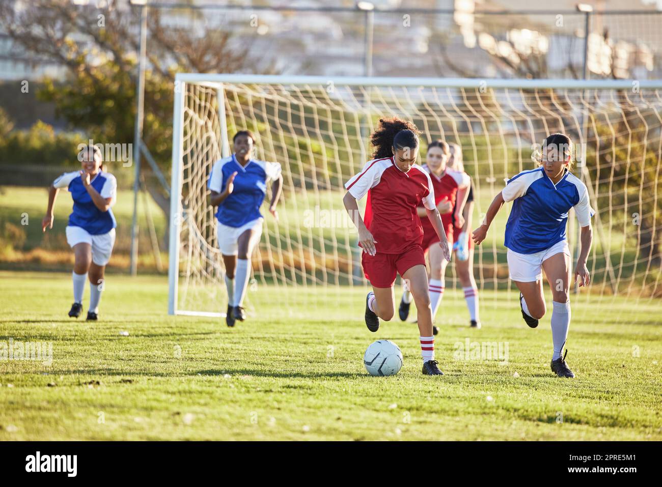 Sports team, girl soccer and kick ball on field in a tournament. Football, competition and athletic female teen group play game on grass. Fit adolescents compete to win match at school championship. Stock Photo