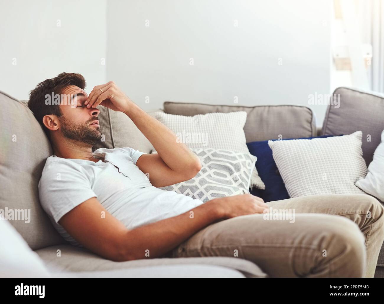 Today, Im going nowhere. a handsome young man holding his nose while lying on a couch at home during the day. Stock Photo