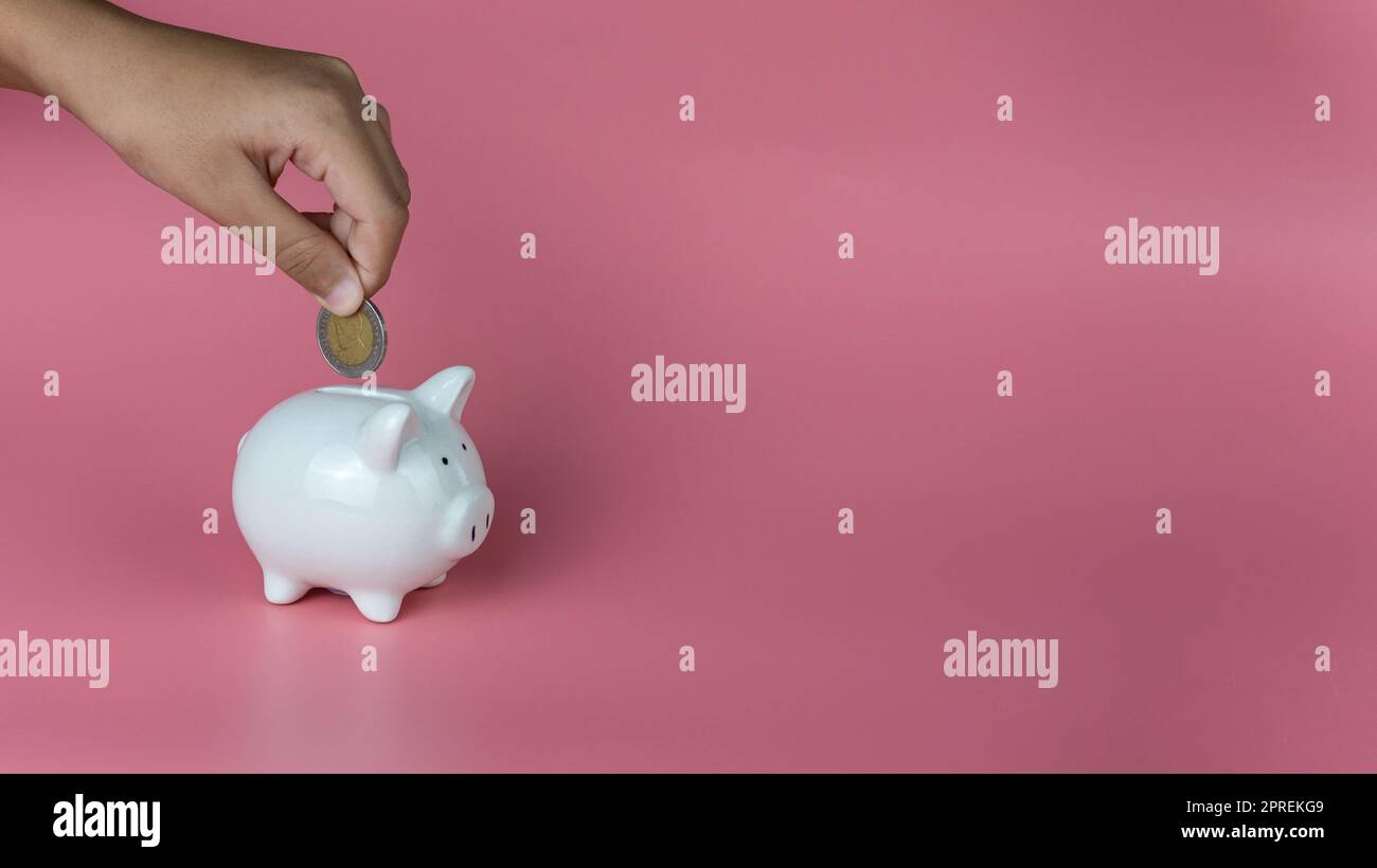 A human hand put a coin in a piggy bank on a pink background. Savings ...