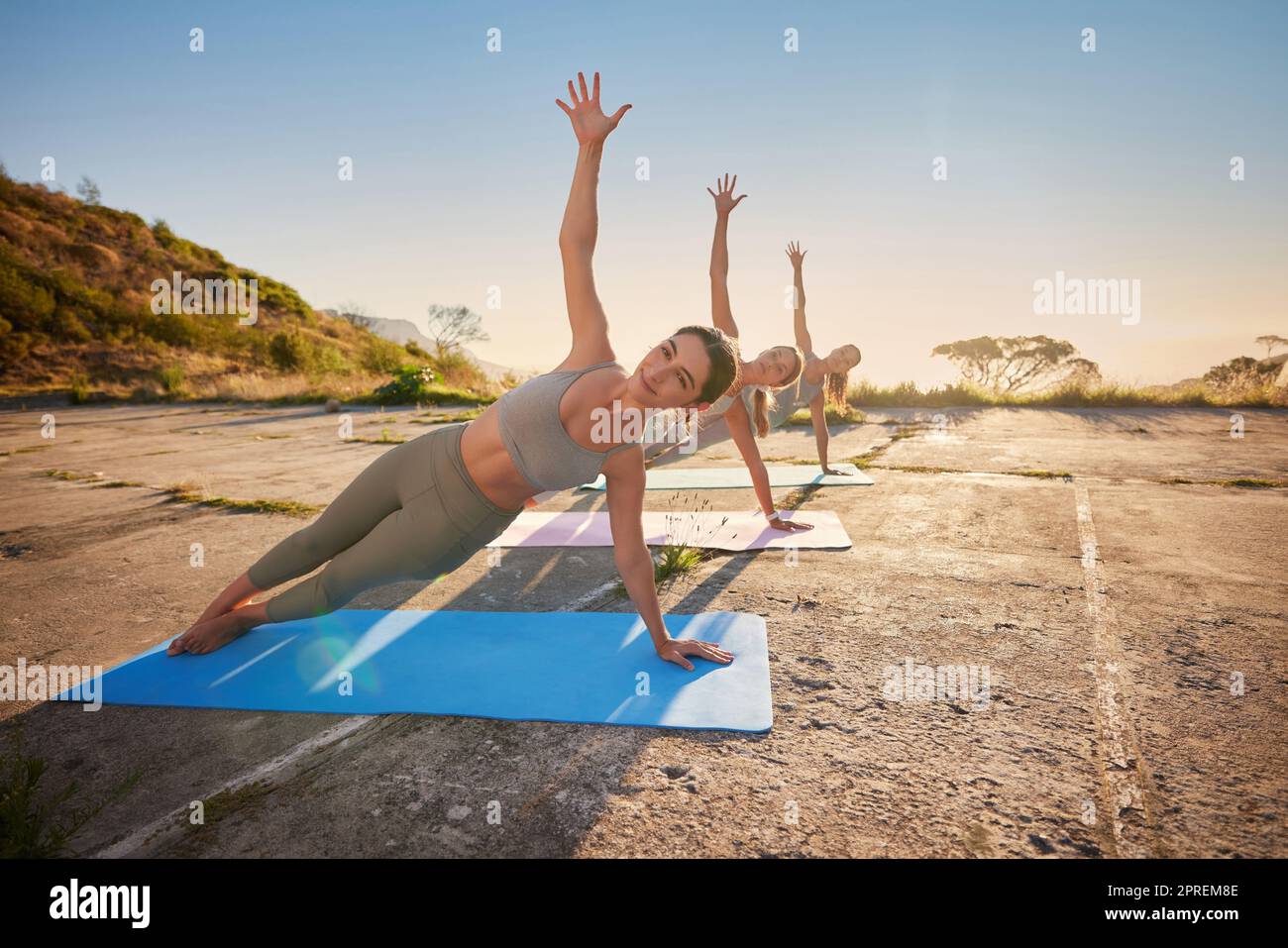 Full length yoga women holding side plank pose in outdoor practice in remote nature. Diverse group of serious beautiful friends using mats and balanci Stock Photo