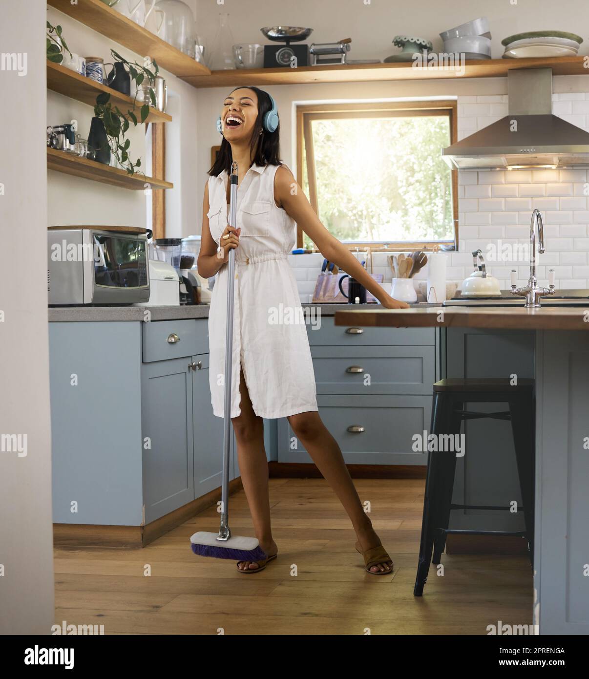 Cleaning, singing and listening to music in a kitchen with headphones. Black woman at home doing