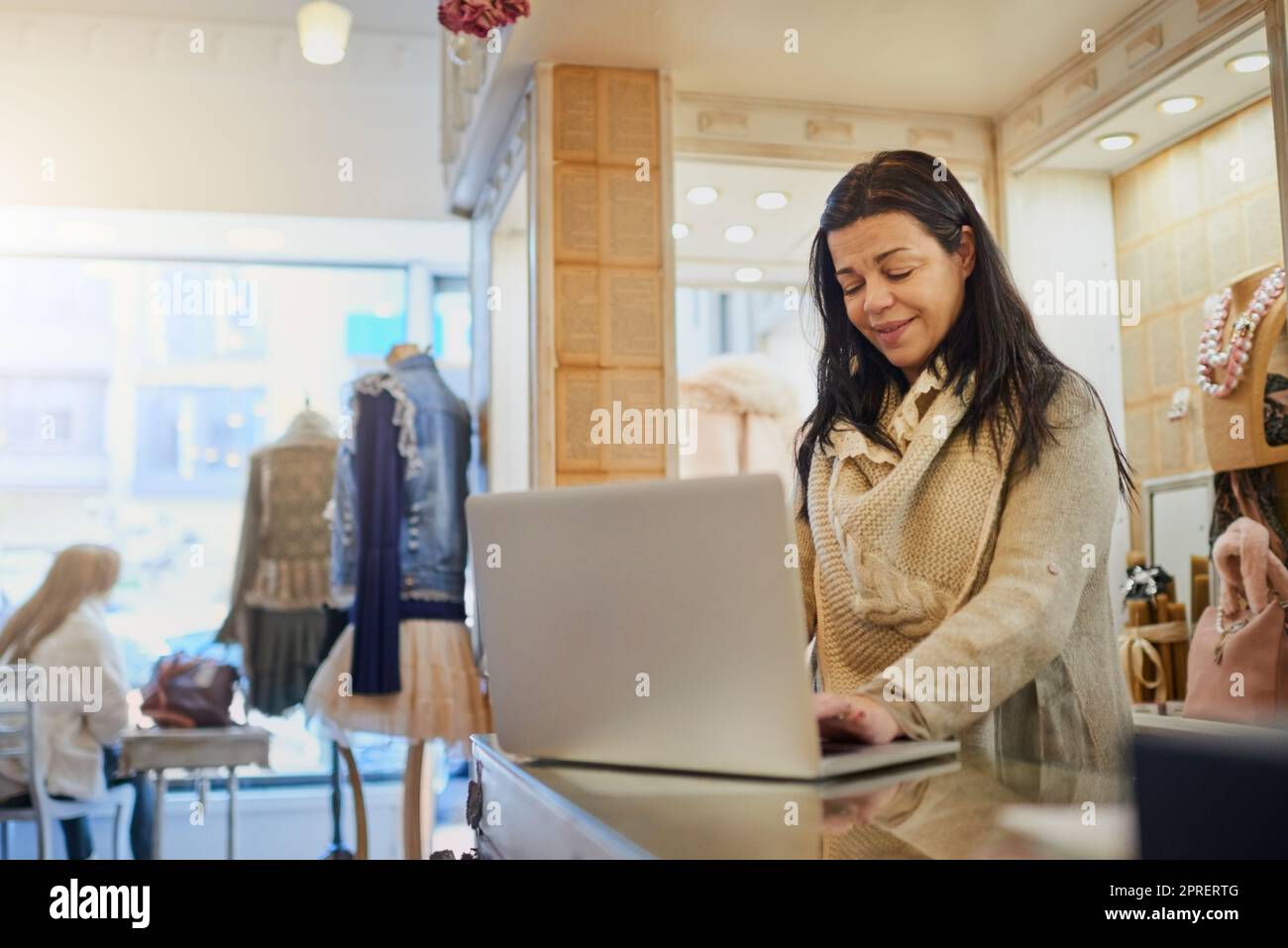 Using online resources to manage her business. an attractive mature female entrepreneur working on a laptop in her self-owned boutique. Stock Photo