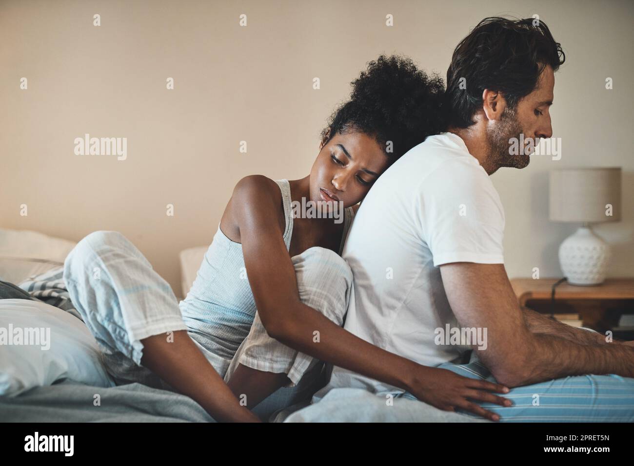 Woman tries to embrace her husband with affection after their fight at home. Unhappy interracial couple with marriage problems forgive each other. Empathy and guilty feelings after the affair. Stock Photo