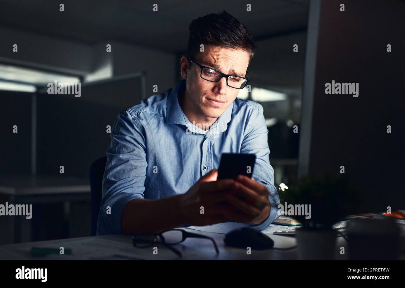 Confused businessman texting on his phone at the office at night. Handsome, confident and corporate caucasian male looking at messages from coworkers while working overtime and feeling unsure Stock Photo