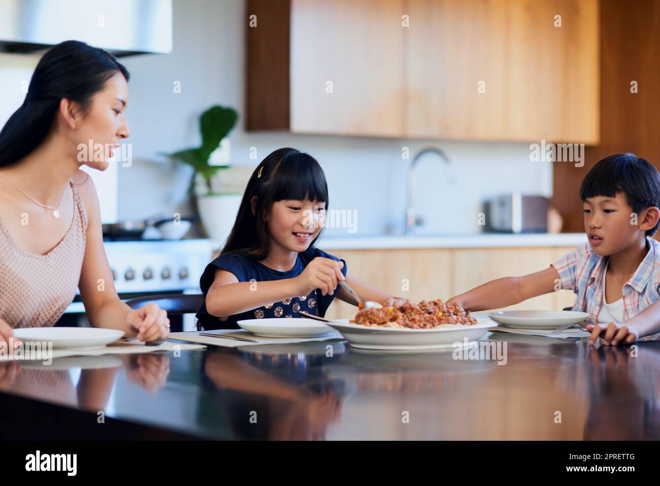 Mom made our favourite meal. two little children enjoying a meal with their mother at home. Stock Photo
