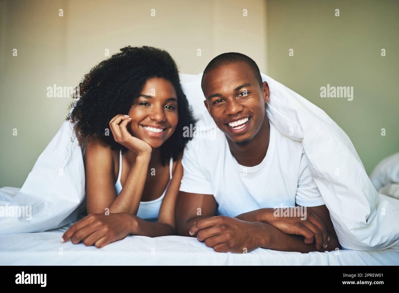 Love starts the day with a smile. Portrait of a happy young couple relaxing under a duvet in their bedroom. Stock Photo