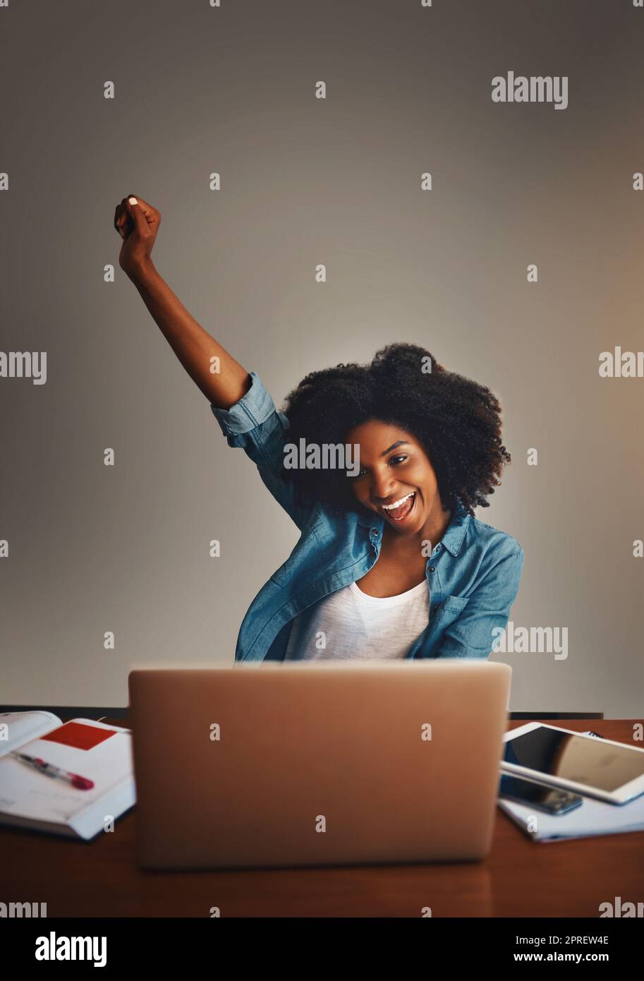 I did it again. Studio shot of an attractive young woman cheering while working on a laptop against a dark background. Stock Photo