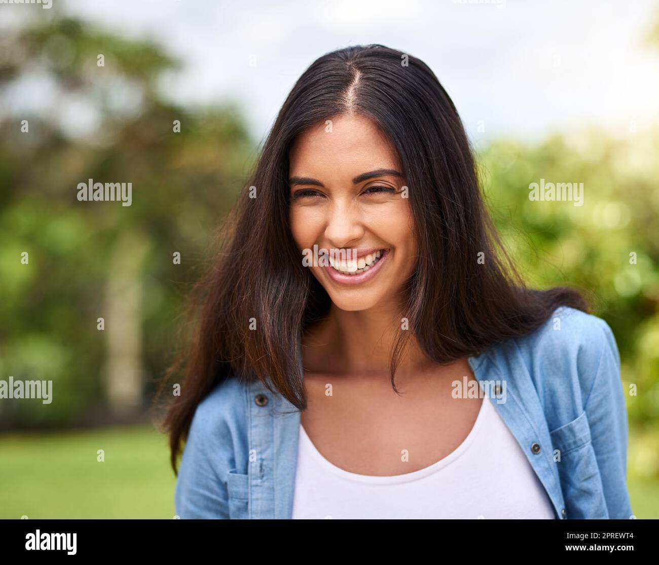She smiles because shes happy. an attractive young woman standing outdoors. Stock Photo