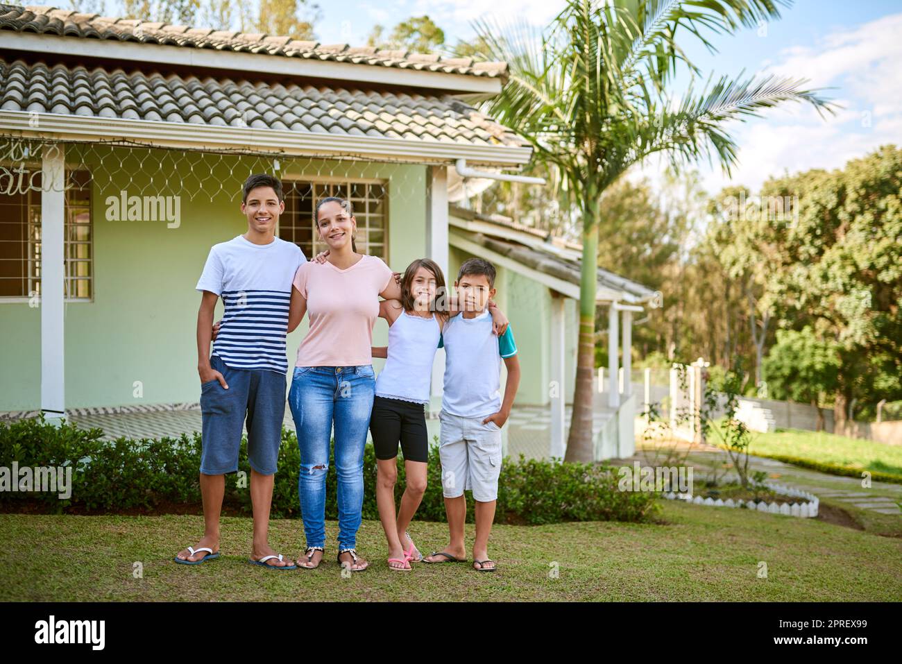 Life can be many things but family makes it true. Portrait of a happy young woman standing together with her daughter and sons in their backyard. Stock Photo